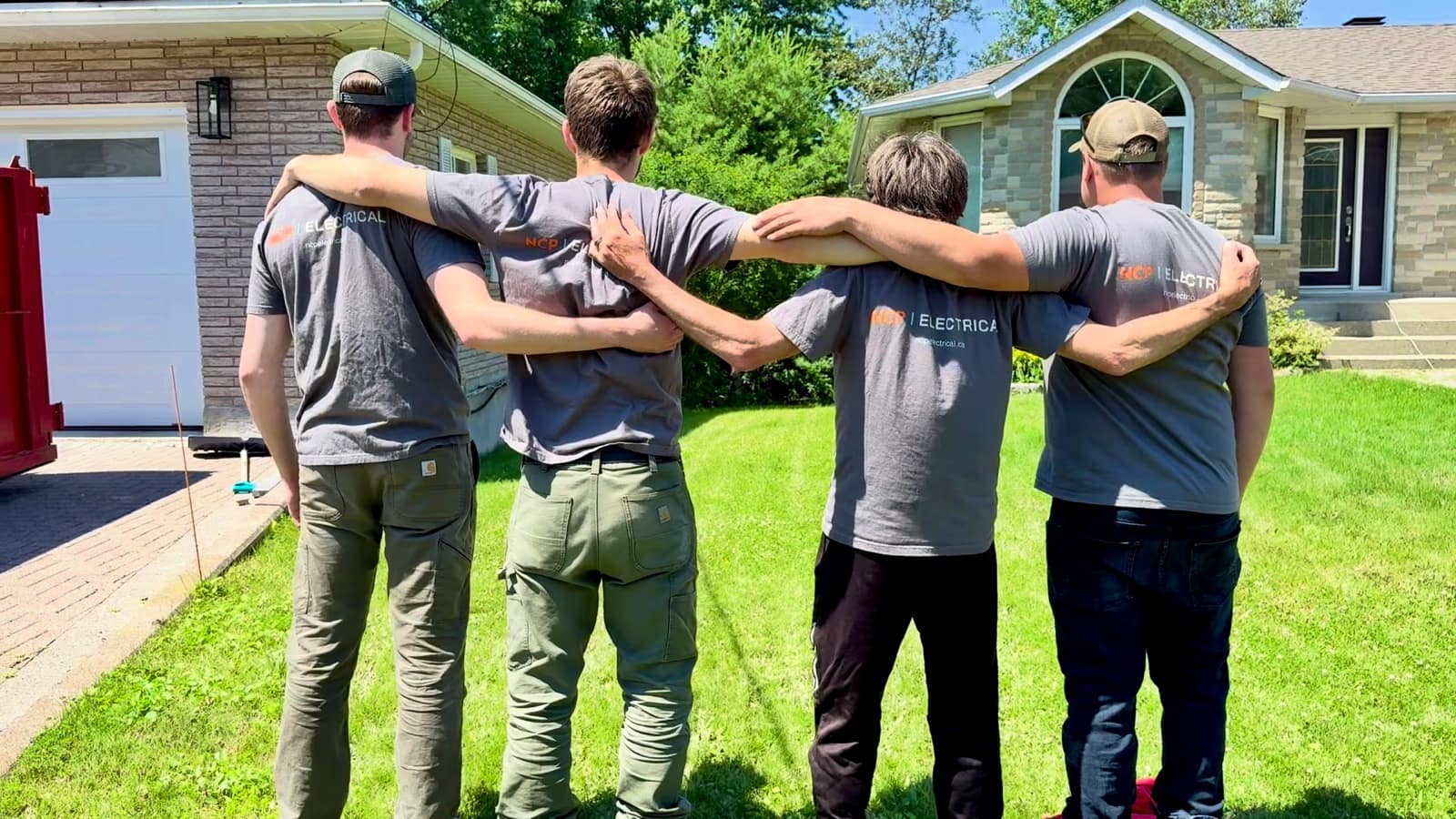 The NCP Electrical crew standing together, arms around each other, looking at a Greater Sudbury home they just finished